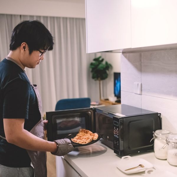 Ein Person stellt ein St&uuml;ck Pizza in eine Mikrowelle.
