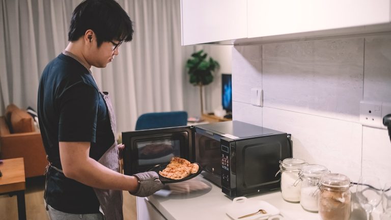 Ein Person stellt ein Stück Pizza in eine Mikrowelle.