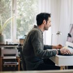 Eine Person sitzt vor einem iMac. Im Hintergrund ist ein Multifunktionsdrucker zu sehen.