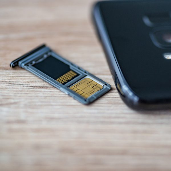 Ein SIM-Karten-Schlitten liegt neben einem Smartphone. In dem Schlitten sind eine SIM- und eine SD-Karte eingelegt.