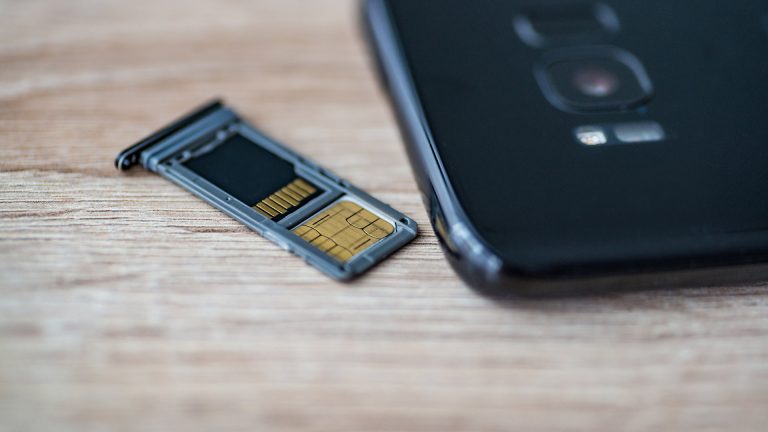 Ein SIM-Karten-Schlitten liegt neben einem Smartphone. In dem Schlitten sind eine SIM- und eine SD-Karte eingelegt.