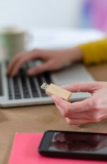 Eine Person hält einen USB-Stick in der Hand und sitzt vor einem Laptop.