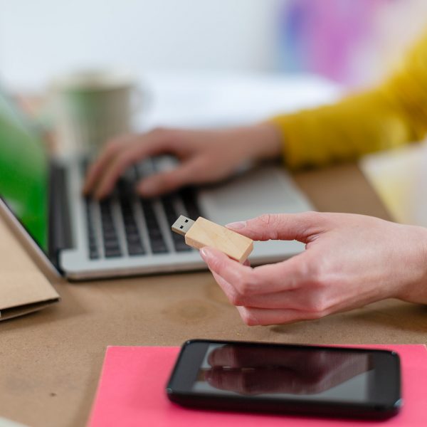 Eine Person h&auml;lt einen USB-Stick in der Hand und sitzt vor einem Laptop.