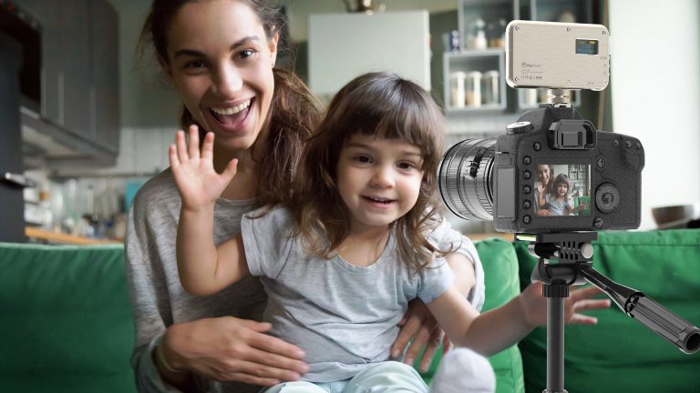 Eine Person hat ein Kind auf dem Schoss. Die beiden lächeln in eine Kamera, die vor ihnen steht.