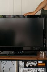 Eine Person schaut hinter einen Fernseher, der auf einem Holztisch steht.