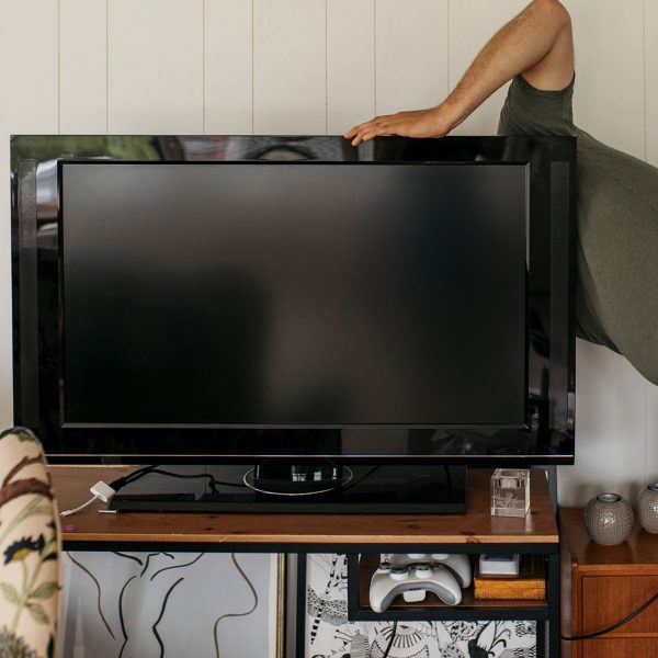 Eine Person schaut hinter einen Fernseher, der auf einem Holztisch steht.