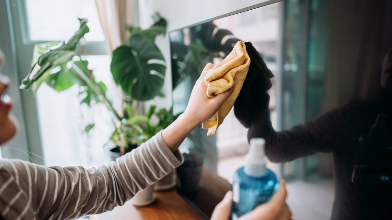 Eine Person reinigt den Bildschirm eines Fernsehers mit einem Tuch.