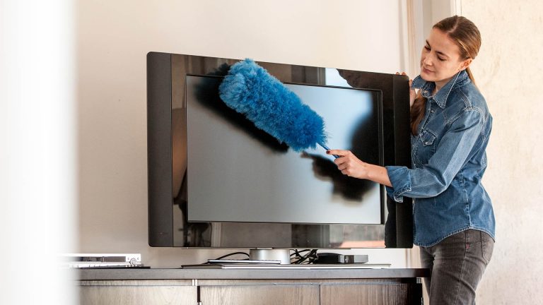 Eine Person macht mit einem Staubwedel einen Fernseher sauber.