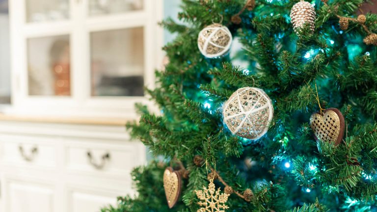 An einem Weihnachtsbaum leuchtet eine Lichterkette in Türkis, im Hintergrund steht ein Buffetschrank.