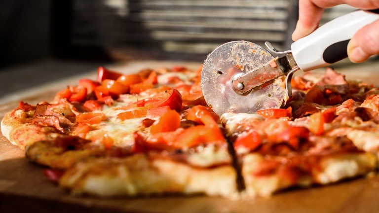 Ein Pizzaschneider fährt über eine Pizza und schneidet sie in handgerechte Stücke.