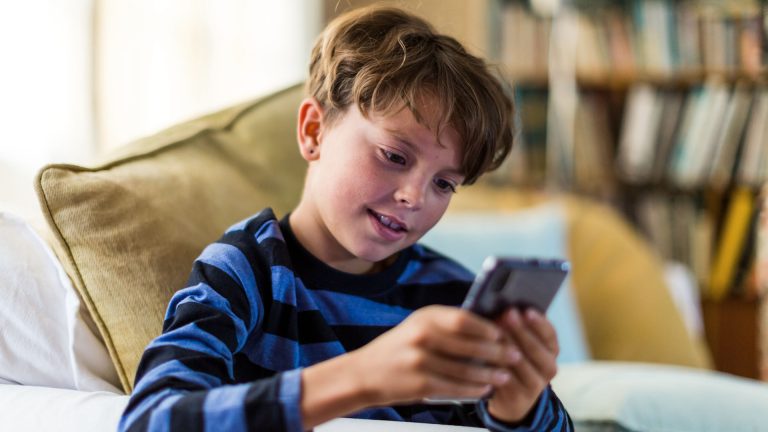 Ein Kind sitzt auf einem Sofa und spielt dabei auf einem Smartphone.