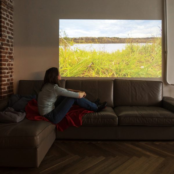 Eine Person sitzt auf einem Sofa vor der Projektion eines Beamers.
