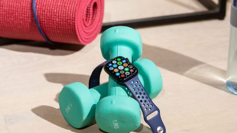 Eine Apple Watch mit blauem Sportarmband liegt über ein paar Hanteln.