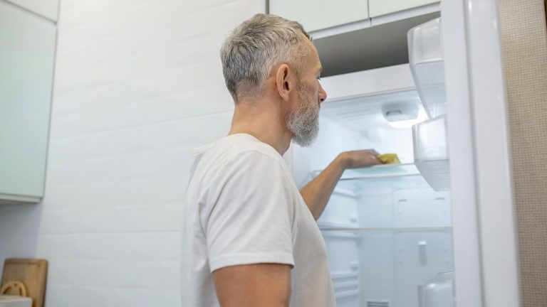 Eine Person wischt einen leeren Kühlschrank mit einem Lappen aus.
