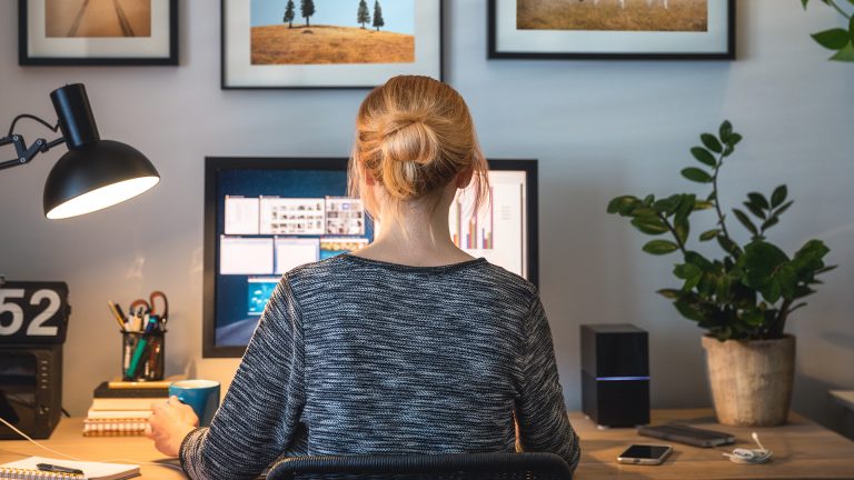 Eine Person sitzt an einem Schreibtisch vor einem Bildschirm und arbeitet.