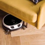 Ein Saugroboter guckt unter einem Sofa hervor.