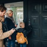 Eine Familie mit Vater, Mutter Kind steht vor ihrer Haustür, an der sich ein smartes Türschloss befindet.