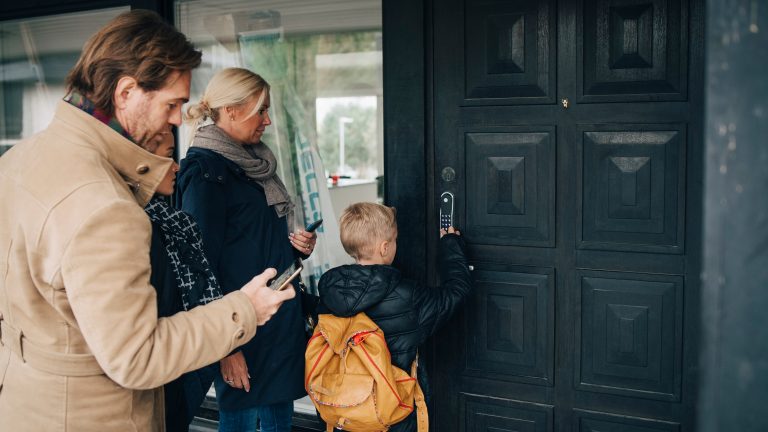 Eine Familie mit Vater, Mutter Kind steht vor ihrer Haustür, an der sich ein smartes Türschloss befindet.