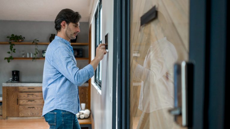 Ein Mann steht vor einer Wand, an der ein Display hängt, über das er seine Smart Home-Geräte programmiert.