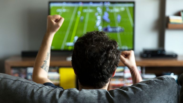 Eine Person schaut ein Football-Match auf einem Fernseher.