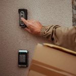 Ein Paketbote bet&auml;tigt eine Funkklingel an einer Hausfassade.