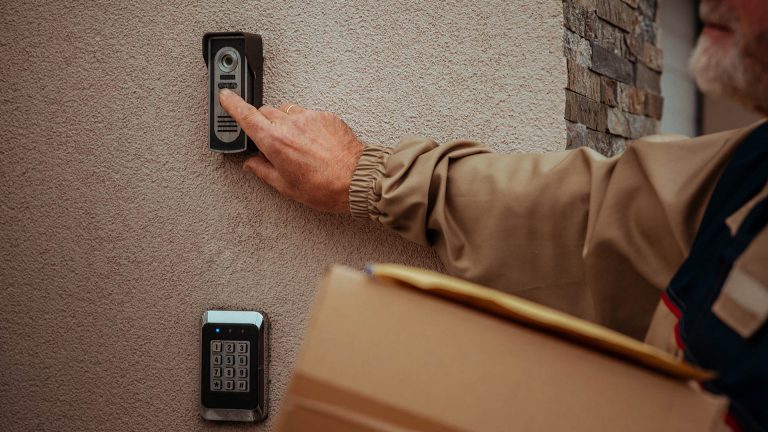 Ein Paketbote betätigt eine Funkklingel an einer Hausfassade.