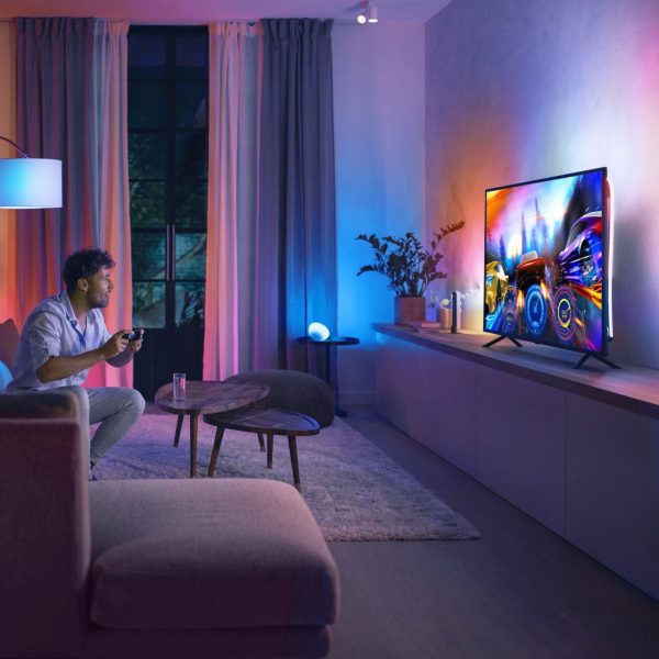 Eine Person sitzt vor einem Fernseher, an dessen R&uuml;ckseite Hue Play Gradient angebracht ist.