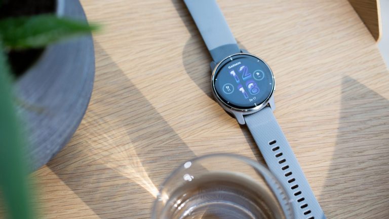 Eine Garmin Venu 2 liegt auf einem Tisch neben einem Wasserglas und einer Gr&uuml;npflanze.