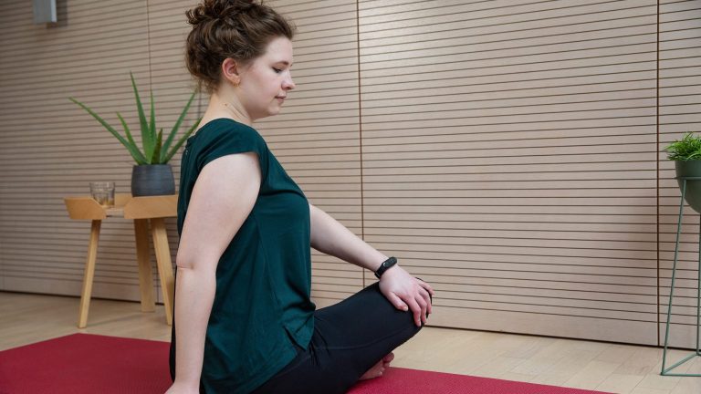 Eine Person macht eine Übung auf einer Yoga-Matte, am linken Handgelenk trägt sie eine Smartwatch.