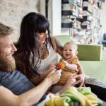 Eltern und ihr kleines Baby sitzen zusammen auf einem Sofa.