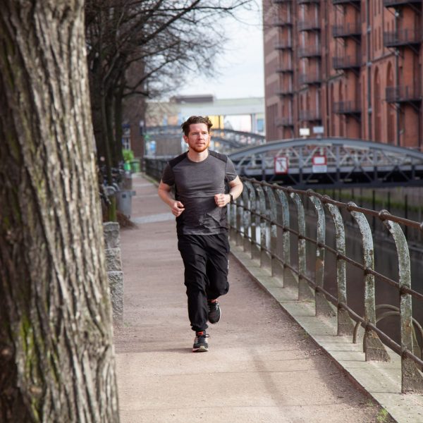 Eine Person l&auml;uft in der Speicherstadt in Hamburg an der Stra&szlig;e entlang und tr&auml;gt dabei einen Fitnesstracker.
