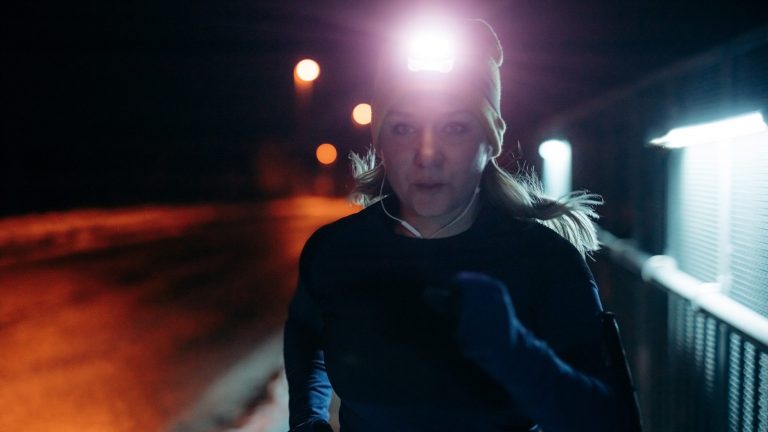 Eine Person mit einer Stirnlampe läuft durch eine winterliche Stadtkulisse.