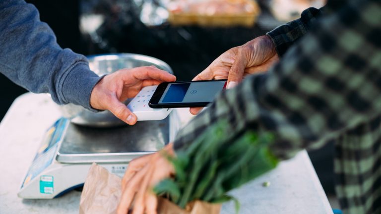 Eine Person zahlt mit einem Smartphone an einem Marktstand.