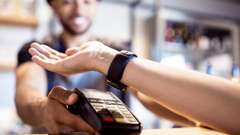 Eine Person hält die Smartwatch an ihrem Arm an ein Kartenterminal.
