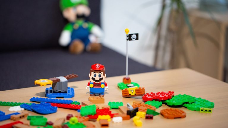 Einige Teile samt Figur von Lego Super Mario auf einem Tisch verteilt.