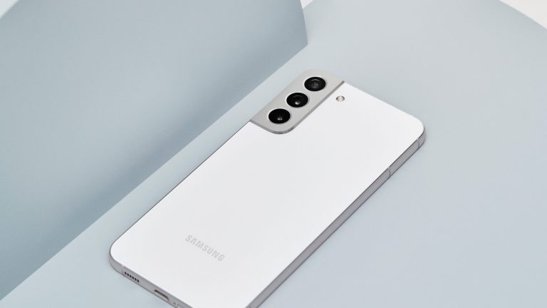 Ein weißes Samsung Galaxy S22 liegt dekorativ auf einer grauen Unterlage.