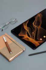 Ein Samsung Galaxy Tab S8 liegt neben einem S Pen, einem Notizbuch und einer Brille.