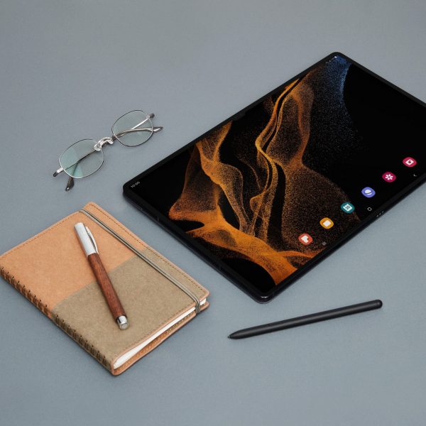 Ein Samsung Galaxy Tab S8 liegt neben einem S Pen, einem Notizbuch und einer Brille.