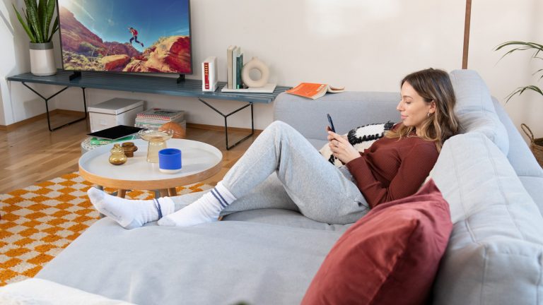 Eine Person liegt auf einem Sofa, neben ihr sind auf einer TV-Bank ein Fernseher und eine FRITZBox_6690_Cable zu sehen.