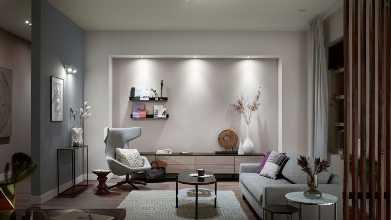 Blick in ein möbliertes Wohnzimmer. Von der Decke und den Wänden illuminieren “White Ambience”-Birnen von Philips Hue den Raum in einem tageslichtähnlichen Weiß.