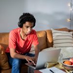 Eine Person mit Kopfh&ouml;rern auf dem Kopf sitzt vor einem MacBook.