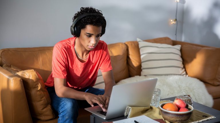 Eine Person mit Kopfhörern auf dem Kopf sitzt vor einem MacBook.
