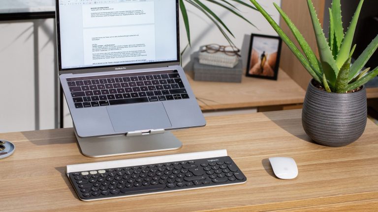 Blick auf einen Schreibtisch mit einer Vollformat-Tastatur vor einem MacBook.