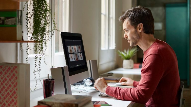 Eine Person sitzt am Schreibtisch vor einem Rechner.