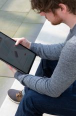Screenshot am iPad Eine Person sitzt auf einer Treppe und schaut auf ein iPad Pro.