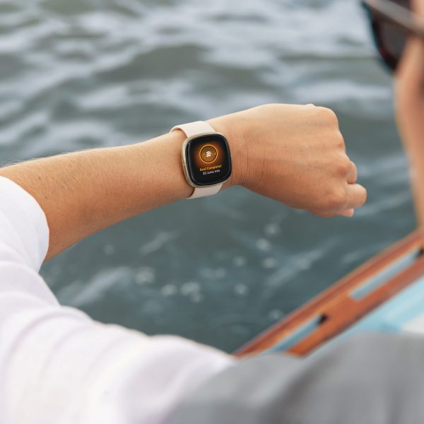 Eine Person sitzt in einem Boot und blickt auf ihren linken Arm, an dem sich ein Fitness-Tracker befindet.