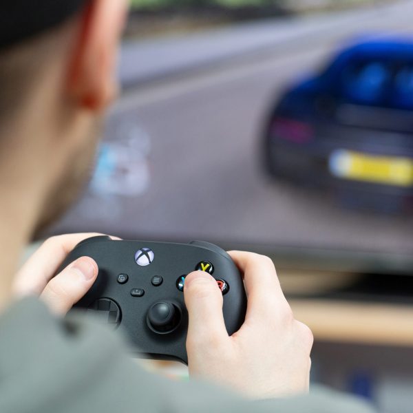 Eine Person sitzt mit einem Controller vor einem Bildschirm und spielt Autorennen.