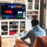 Auf einem Sofa sitzen zwei Personen und schauen auf den Bildschirm ihres Smart-TVs.