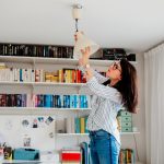 Eine Person steht erh&ouml;ht an einer Deckenlampe und dreht die Gl&uuml;hlampe heraus.
