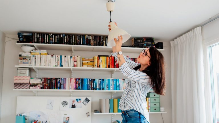Eine Person steht erhöht an einer Deckenlampe und dreht die Glühlampe heraus.